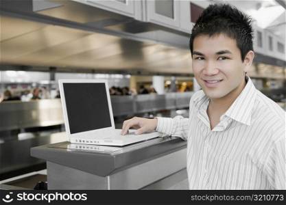 Close-up of a young man using a laptop at an airport and smiling