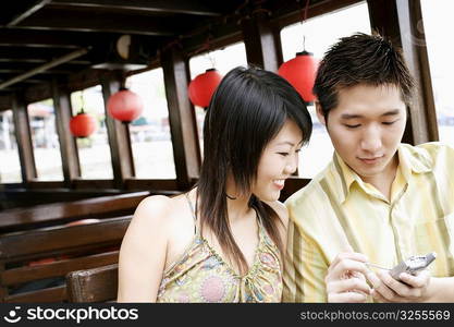 Close-up of a young man using a mobile phone beside a young woman