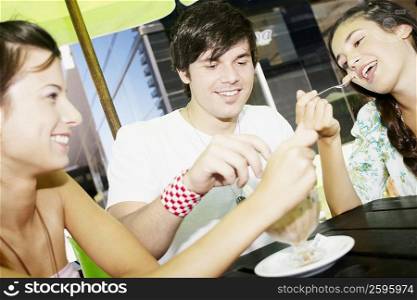 Close-up of a young man with two young women sharing an ice-cream sundae