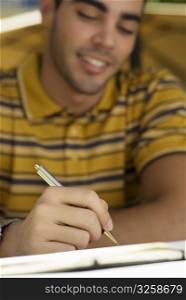 Close-up of a young man writing on a diary and smiling