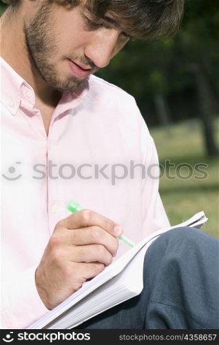 Close-up of a young man writing with a pen in a notepad