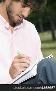 Close-up of a young man writing with a pen in a notepad