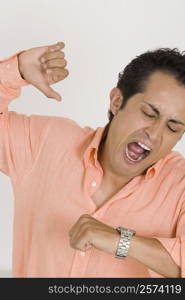 Close-up of a young man yawning after checking the time on his wristwatch