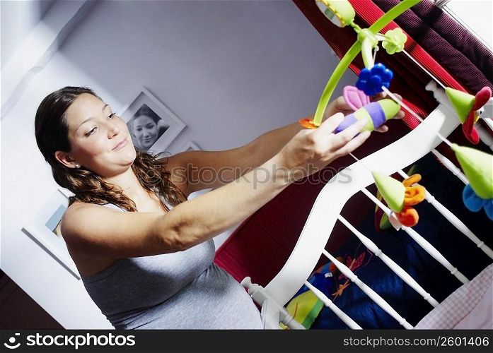 Close-up of a young pregnant woman adjusting toys in a crib
