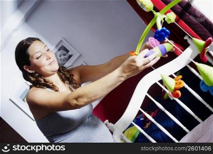 Close-up of a young pregnant woman adjusting toys in a crib