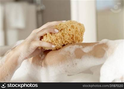 Close-up of a young woman&acute;s hands scrubbing her body with a bath sponge