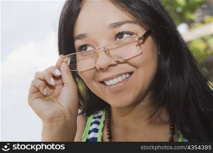 Close-up of a young woman adjusting her eyeglasses and smiling