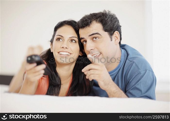 Close-up of a young woman and a mid adult man lying on the bed and watching television