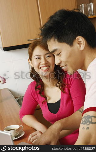 Close-up of a young woman and a mid adult man smiling at a kitchen counter