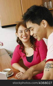 Close-up of a young woman and a mid adult man smiling at a kitchen counter