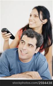 Close-up of a young woman and a mid adult man watching television and smiling