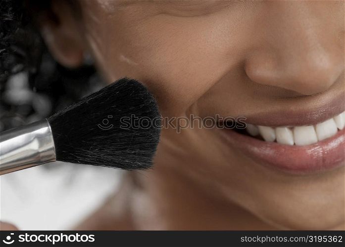 Close-up of a young woman applying blush with a brush
