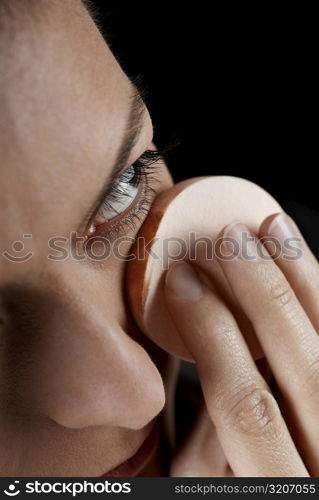 Close-up of a young woman applying face powder with a powder puff