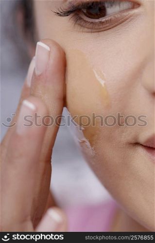 Close-up of a young woman applying honey on her cheek