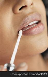 Close-up of a young woman applying lip gloss on her lips