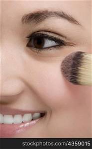 Close-up of a young woman applying make-up and smiling