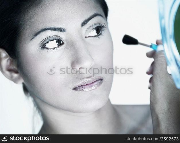 Close-up of a young woman applying make-up with a make-up brush