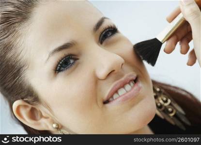 Close-up of a young woman applying make-up with a make-up brush