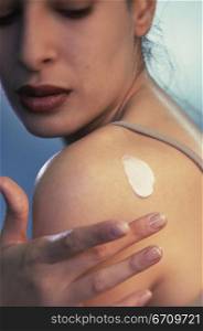Close-up of a young woman applying moisturizer on her shoulder