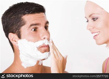 Close-up of a young woman applying shaving cream on a mid adult man&acute;s face