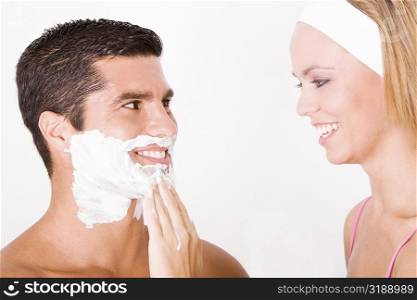 Close-up of a young woman applying shaving cream on a mid adult man&acute;s face