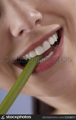 Close-up of a young woman biting a celery stick