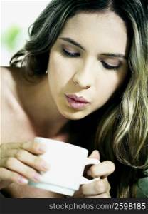 Close-up of a young woman blowing air into a coffee cup