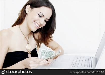 Close-up of a young woman counting dollar bills in front of a laptop