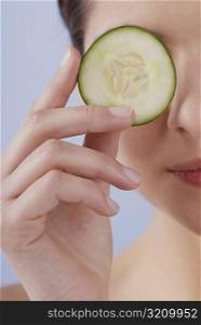Close-up of a young woman covering her eye with a cucumber slice