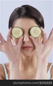 Close-up of a young woman covering her eyes with cucumber slices