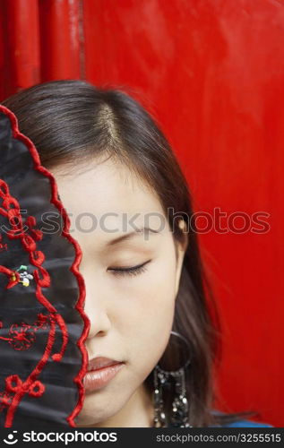 Close-up of a young woman covering her one eye with a folding fan