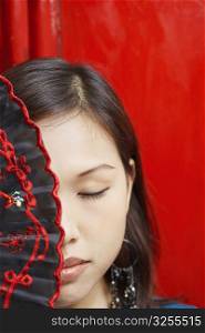 Close-up of a young woman covering her one eye with a folding fan