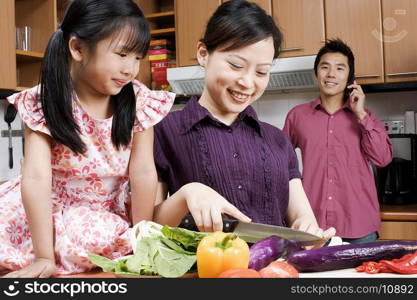 Close-up of a young woman cutting vegetables with her daughter sitting beside her