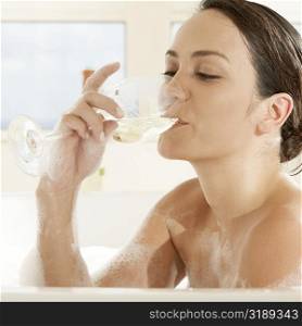 Close-up of a young woman drinking white wine in the bathtub