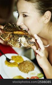 Close-up of a young woman eating a grilled fish