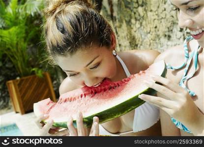 Close-up of a young woman eating a slice of watermelon with another young woman smiling