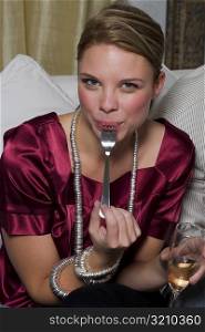 Close-up of a young woman eating food with a fork and holding a champagne flute