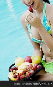 Close-up of a young woman eating fruit at the poolside