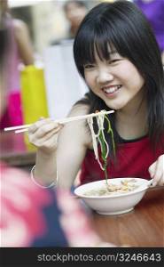 Close-up of a young woman eating noodles with chopsticks