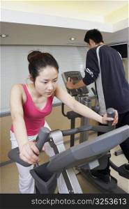 Close-up of a young woman exercising in a gym with a young man
