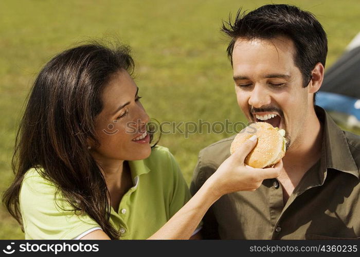 Close-up of a young woman feeding a burger to a young man