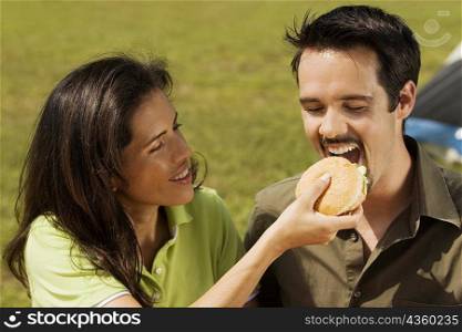 Close-up of a young woman feeding a burger to a young man