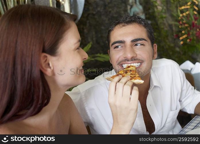 Close-up of a young woman feeding a young man with a pizza slice