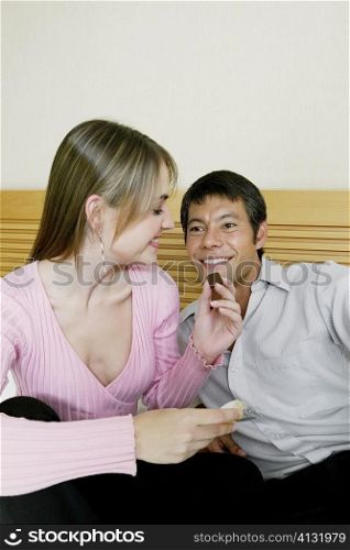 Close-up of a young woman feeding chocolates to a mid adult man