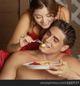 Close-up of a young woman feeding fruit salad to a young man