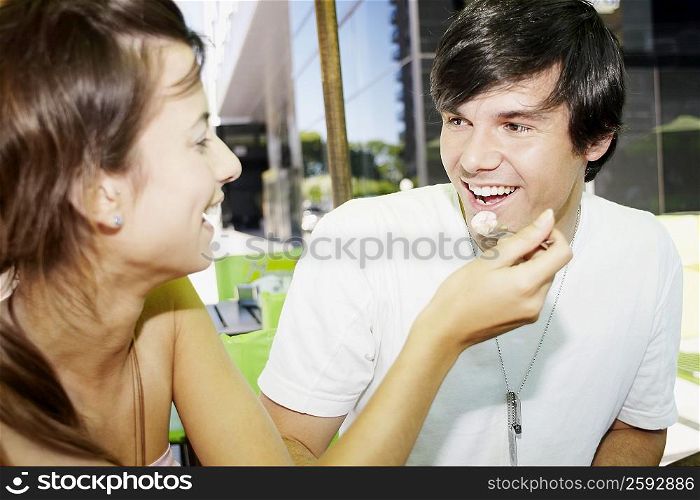 Close-up of a young woman feeding ice-cream to a young man