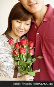 Close-up of a young woman holding a bouquet of red roses and standing with a young man