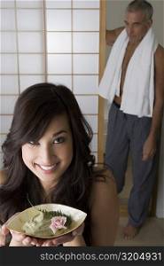 Close-up of a young woman holding a bowl of herb with her father standing behind her