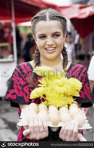 Close-up of a young woman holding a bunch of flowers and an egg carton