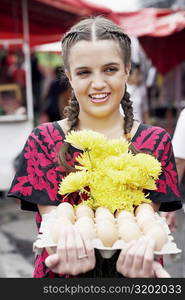 Close-up of a young woman holding a bunch of flowers and an egg carton